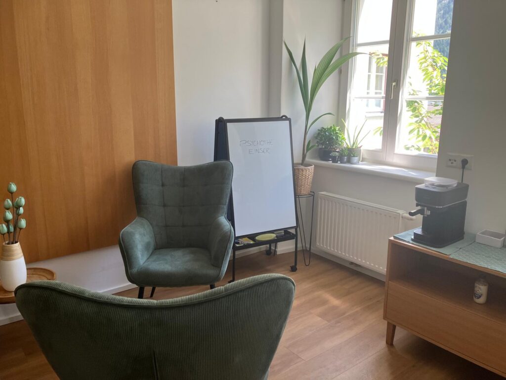 Psychotherapiepraxis - zwei grüne Sessel. Fenster und Kaffeemaschine im Hintergrund