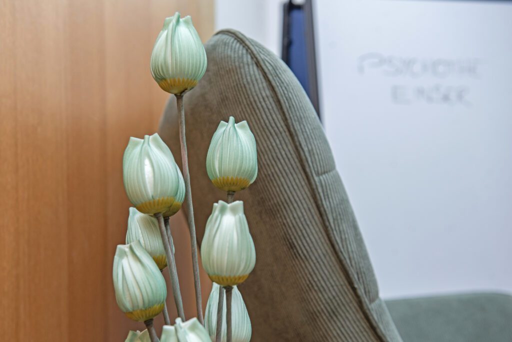 Detailaufnahme einer Vase mit dekorativen Trockenblumen vor einem gemütlichen Therapiesessel